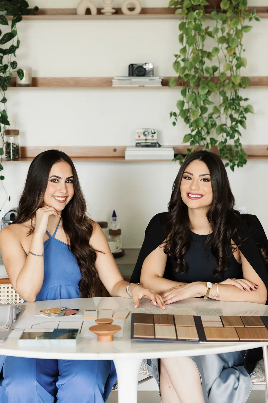 Malu e Laura sorrindo, sentadas à mesa com amostras de materiais